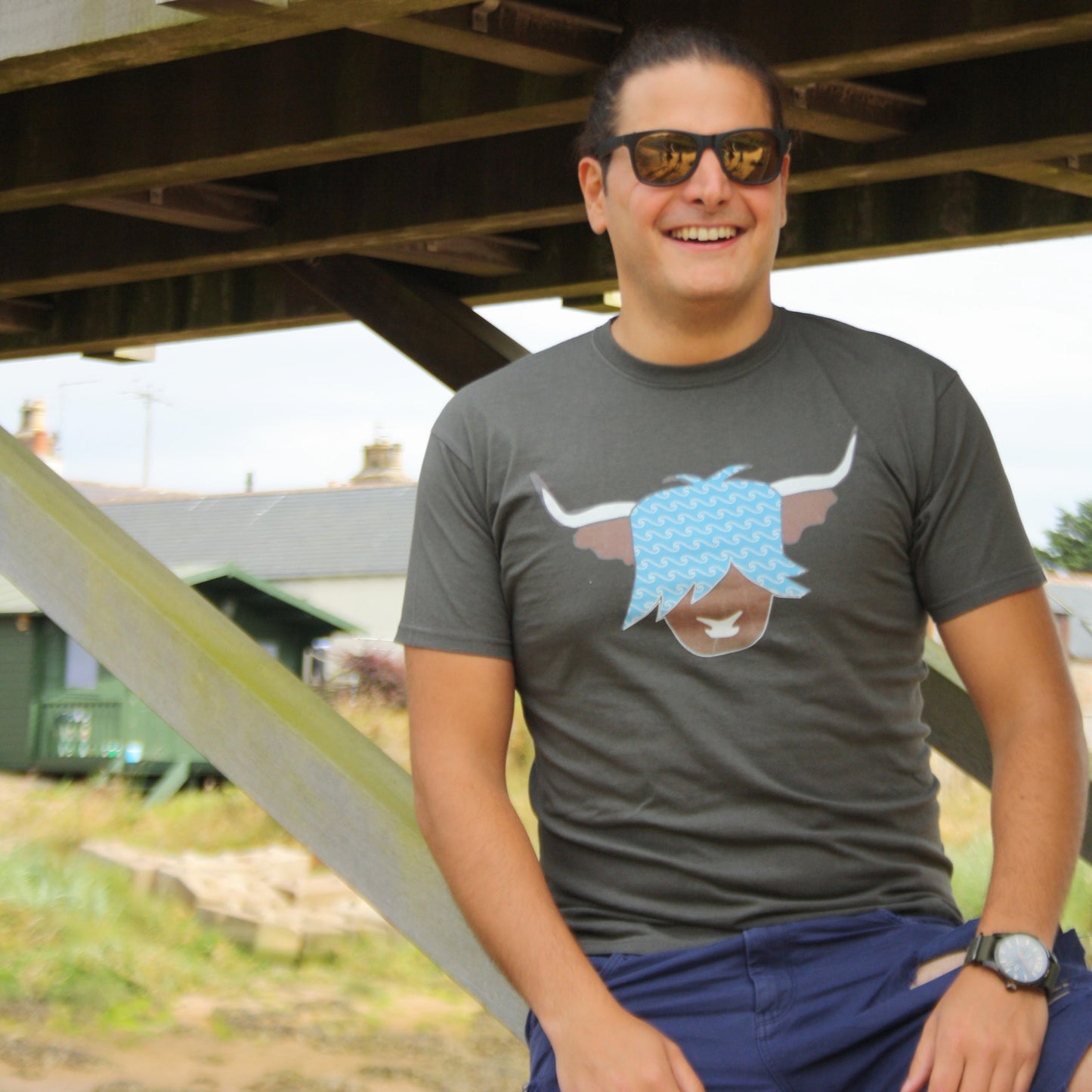 Man wearing a grey highland cow tshirt with the design of a brown highland cow with blue hair and a wave pattern