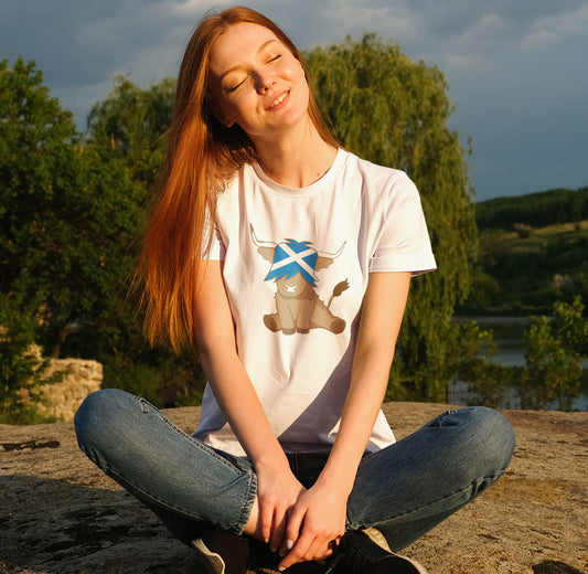 woman with ginger hair enjoying sun while wearing a highland cow t-shirt that contains the scottish flag